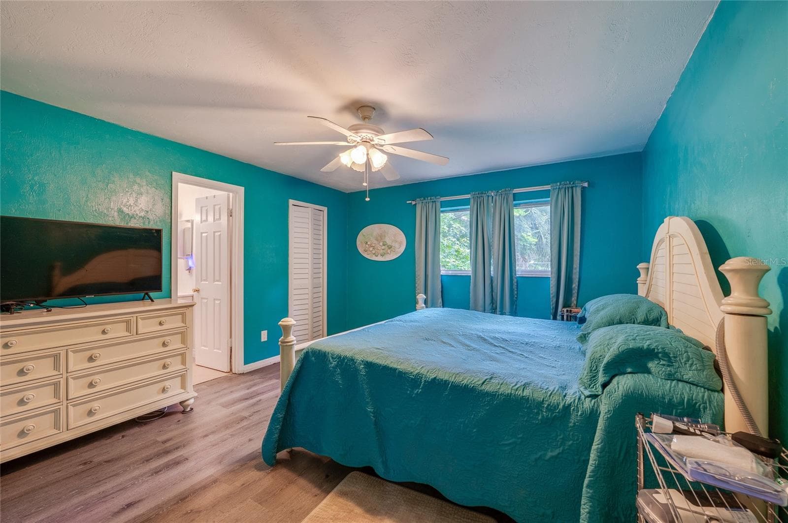 Primary bedroom suite styled with bright turquoise walls, LVP flooring, a white-panel closet, and direct access to an ensuite bathroom. - 146 WESTWOOD DR, DAYTONA BEACH