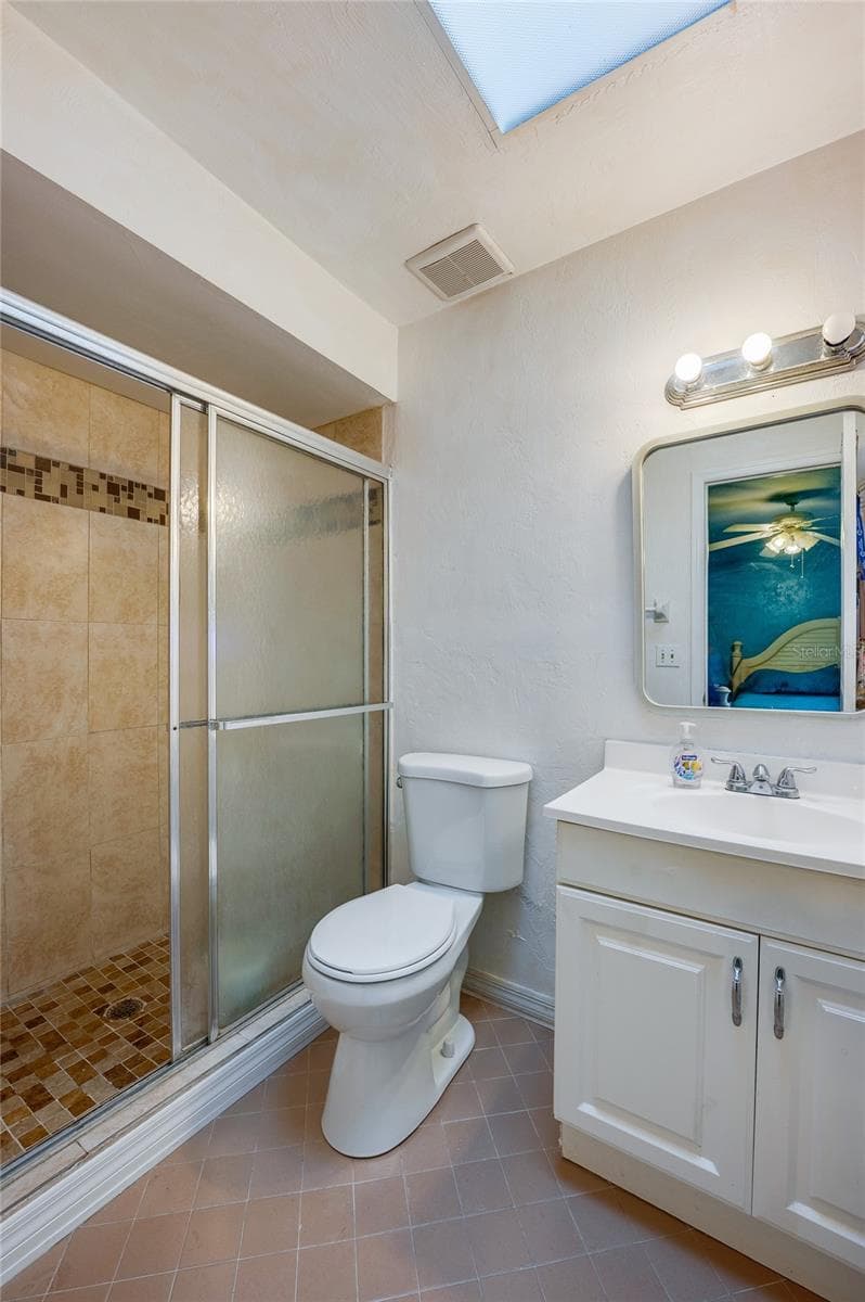 Ensuite bathroom featuring a walk-in shower with tiled surround and glass sliding doors, paired with a white vanity and skylight overhead. - 146 WESTWOOD DR, DAYTONA BEACH