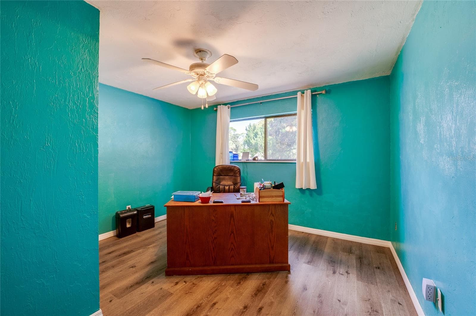 Spacious home office/bedroom featuring vibrant teal walls, low-maintenance LVP flooring, and a large window providing ample natural light. - 146 WESTWOOD DR, DAYTONA BEACH