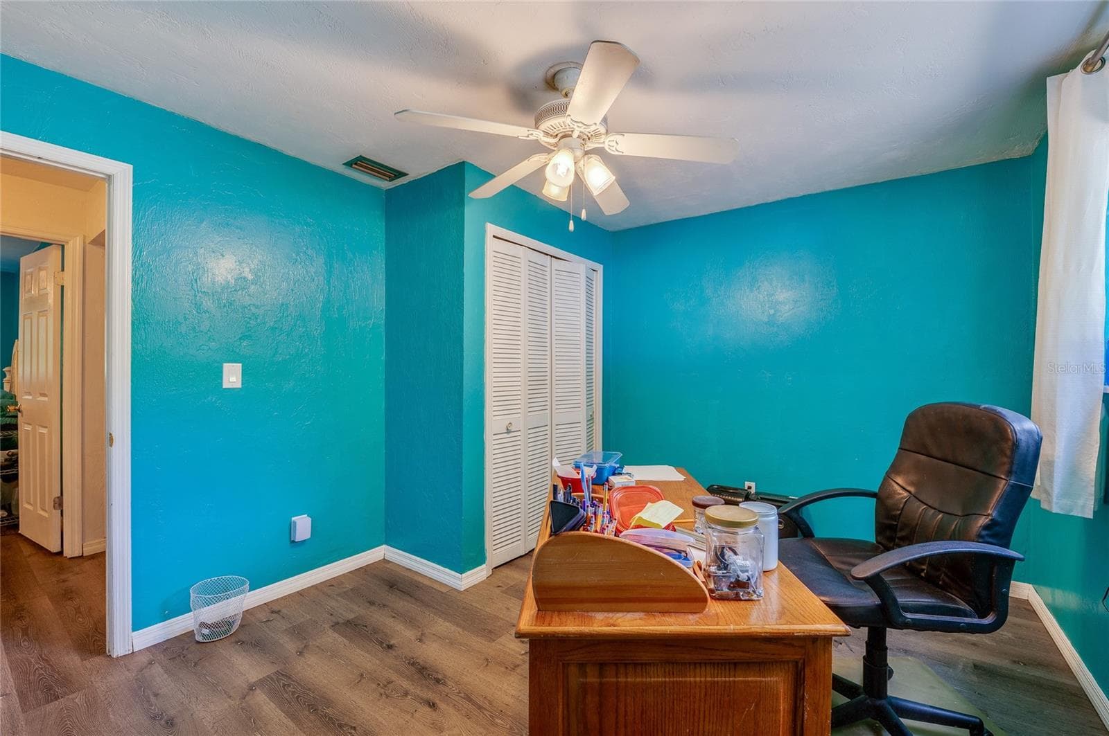 Functional home office/bedroom area illuminated by a ceiling fan, featuring turquoise walls, closet storage, and durable LVP flooring. - 146 WESTWOOD DR, DAYTONA BEACH
