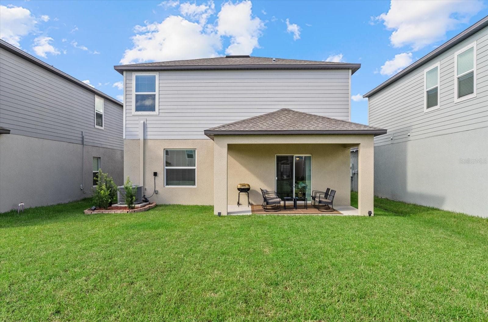 Rear exterior view showcasing the covered patio and generous lawn. - 8431 BELLA MAR TRL, PARRISH