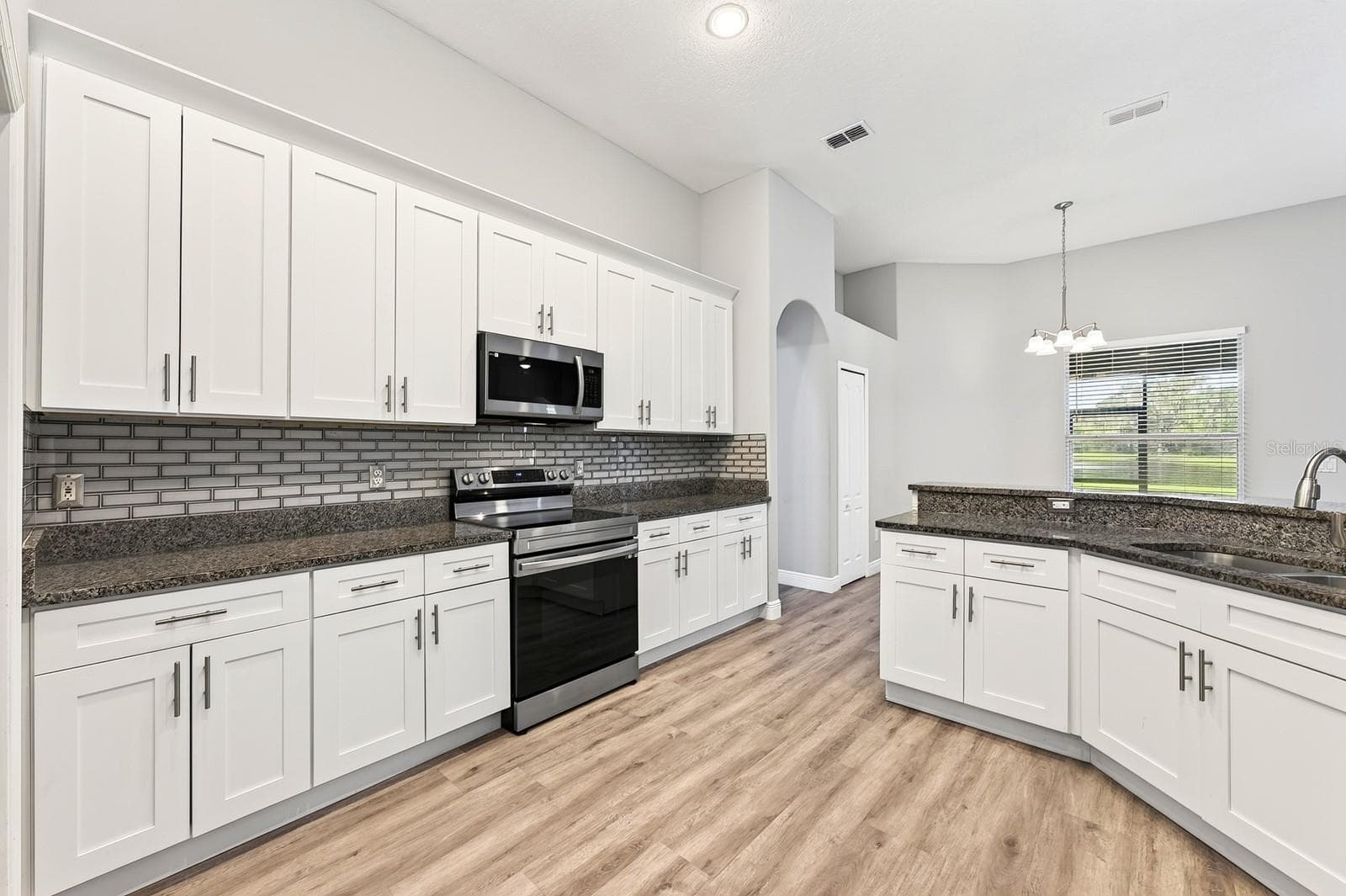 The well-appointed kitchen features GRANITE COUNTERTOPS, timeless cabinetry topped with crown molding, STAINLESS STEEL APPLIANCES, a chic tiled backsplash, breakfast bar and pantry storage. - 4946 LAZY OAKS WAY, ST CLOUD