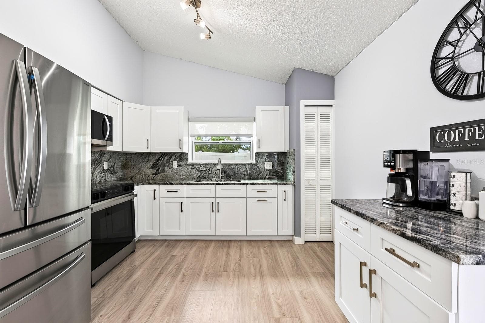 The UPDATED KITCHEN fits right into the OPEN CONCEPT living space with shaker-style cabinetry, STAINLESS STEEL APPLIANCES, a modern color palette, coffee bar, and a window over the sink bringing in additional natural light. - 9905 DEAN ACRE DR, ORLANDO