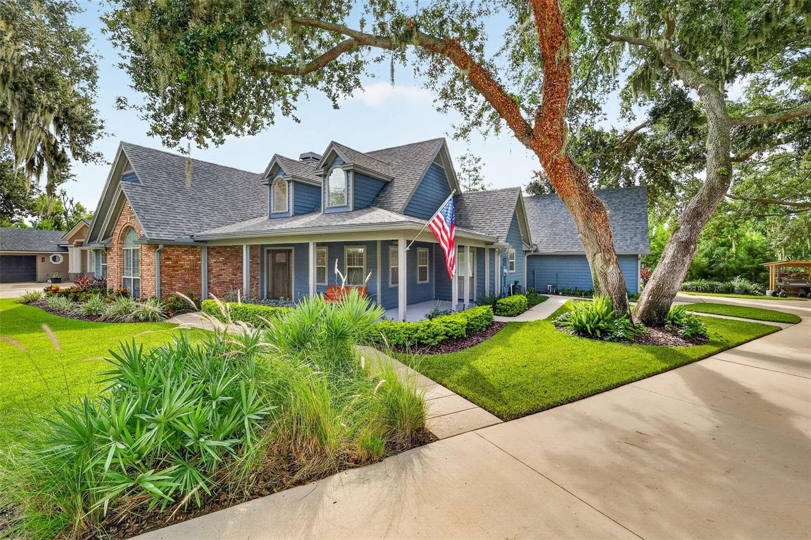 Angled side view of the front of house with covered wraparound front porch under an arching oak tree, - 267 RESERVE DR, TAVARES