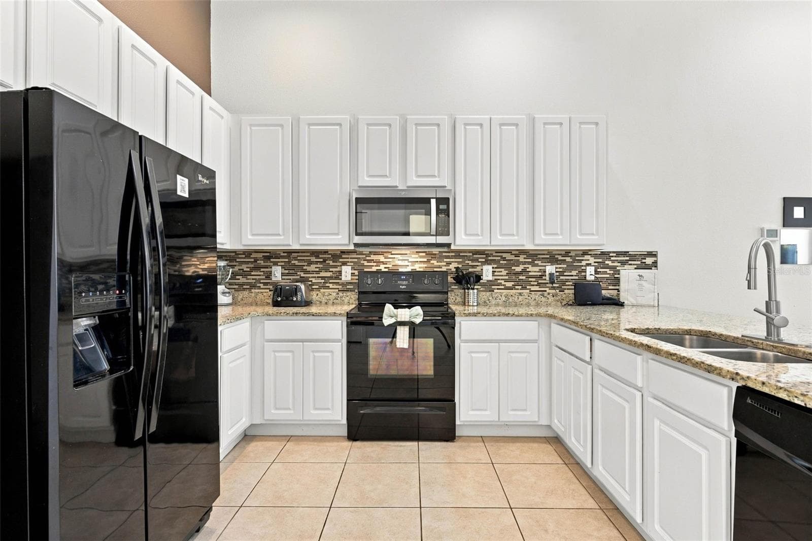 Open kitchen with 42" white cabinets, black Whirlpool appliances and granite countertops. - 337 MARCELLO BLVD, KISSIMMEE