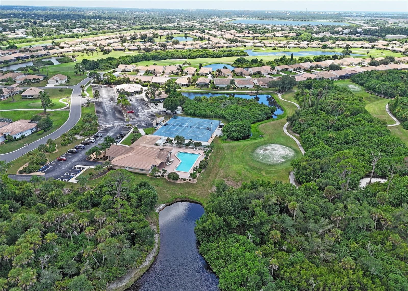 Clubhouse with pool and tennis courts nestled within greenery and water. - 8351 CREEKVIEW LN, ENGLEWOOD