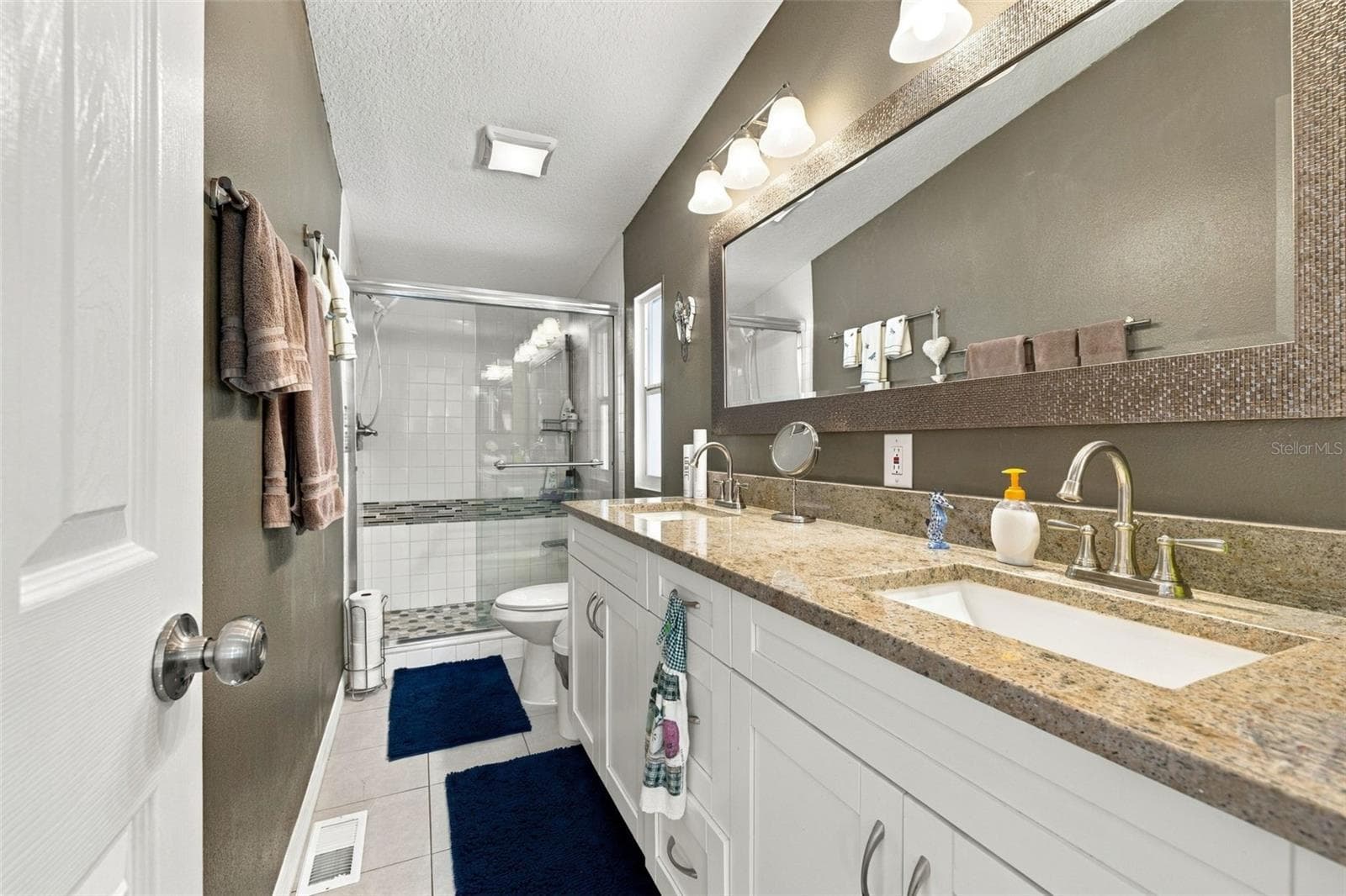 Spa-like ensuite bathroom with a dual sink vanity, updated lighting fixtures, faucets, custom walk-in shower with tempered shower glass doors, comfort height toilet and a designer vanity mirror. - 3041 SHORT LEAF ST, WESLEY CHAPEL