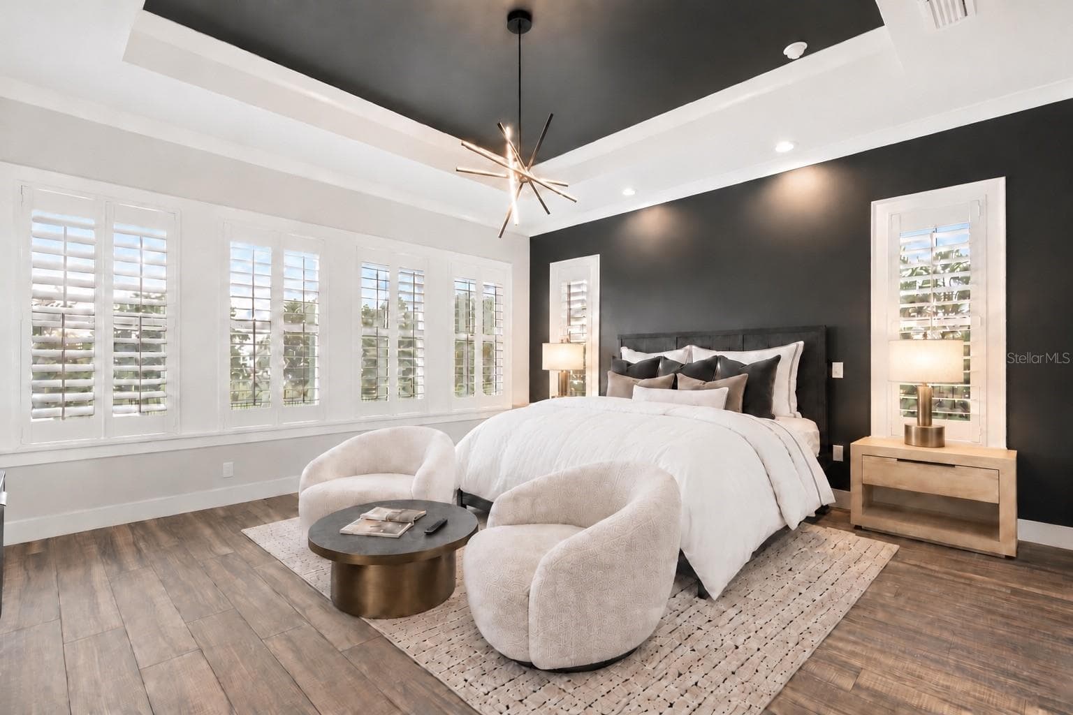 FIRST-FLOOR PRIMARY SUITEFIRST-FLOOR PRIMARY SUITESet within its own rear wing, the 18' × 18' first-floor primary suite features a dramatic tray ceiling, abundant natural light and a private setting apart from the main living spaces.Virtual staged. Bedding, chairs, round table, lamps. - 907 CELADON ST, WINTER GARDEN