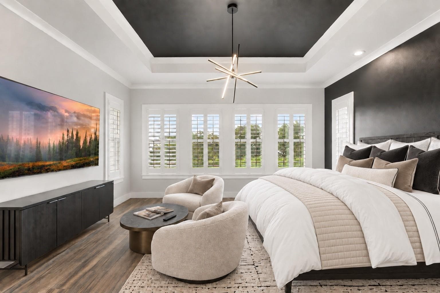 TRAY CEILING + PLANTATION SHUTTERSA recessed tray ceiling and a wall of plantation-shuttered windows give the primary bedroom architectural presence and generous natural light.Virtual staged added: Bedding, chairs, table - 907 CELADON ST, WINTER GARDEN