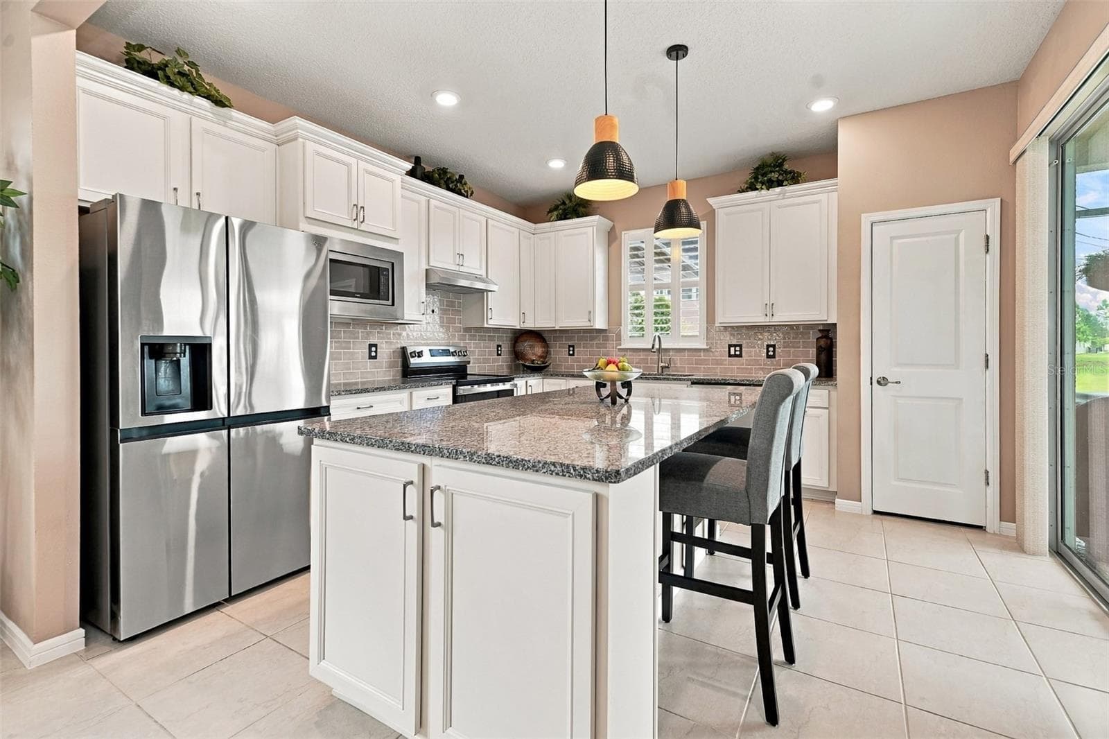 Upgraded kitchen w/granite countertops, SS appliances, tiled backsplash, pantry, center island, pendant lights, window w/shutters & sliding glass door to screened lanai - 5995 SW 93RD CIR, OCALA