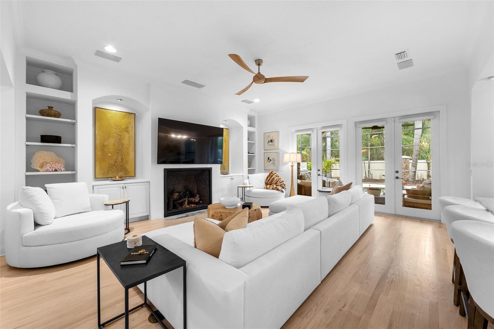 Built-in bookcases flanking the fireplace, French doors with lanai access, and light wood flooring. - 1921 FLORESTA VIEW DR, TAMPA