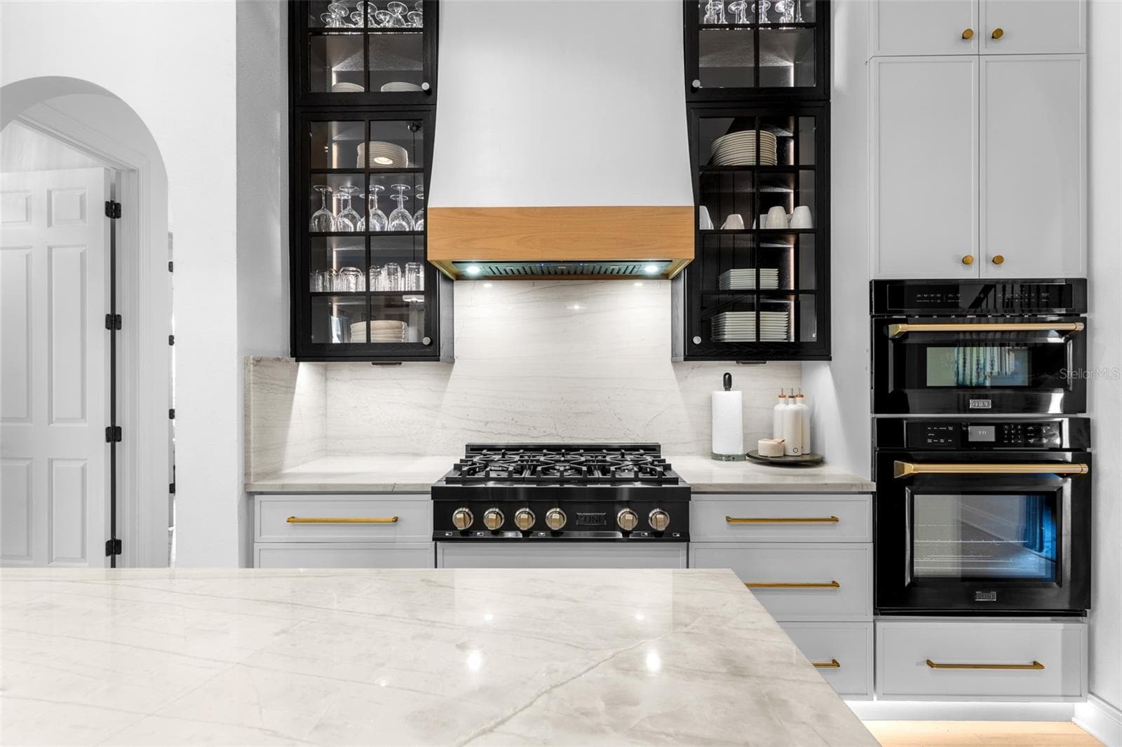 Gas range with wood-trimmed hood, glass-front black upper cabinets, and built-in wall oven and microwave. - 1921 FLORESTA VIEW DR, TAMPA