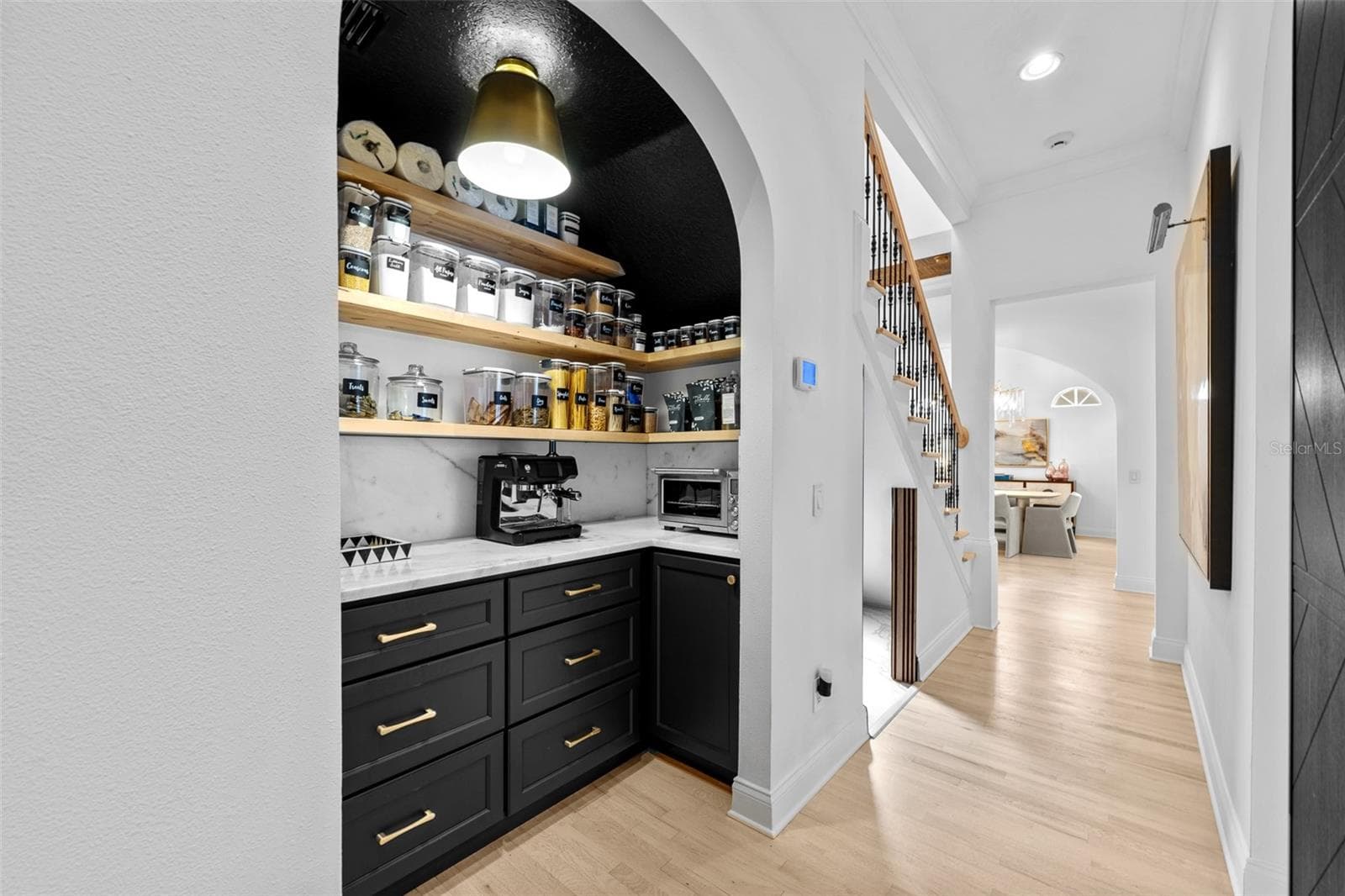 Arched entry to the pantry with black cabinetry, floating wood shelves, and stone countertops. - 1921 FLORESTA VIEW DR, TAMPA