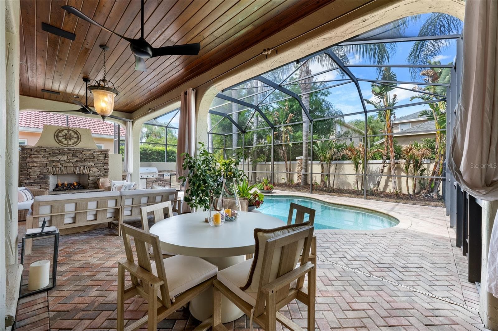 Covered lanai — Wood plank ceiling, ceiling fans, outdoor dining area, stone fireplace, and pool view. - 1921 FLORESTA VIEW DR, TAMPA