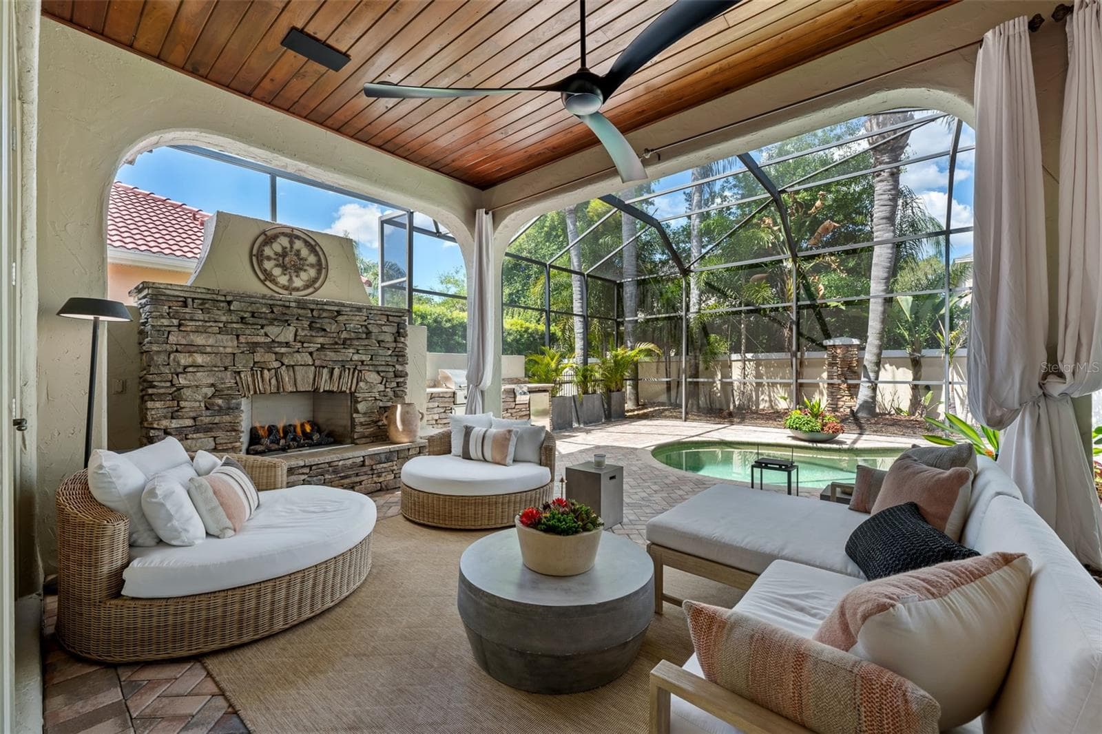 Lounge seating, stacked-stone fireplace, and arched openings to the pool. - 1921 FLORESTA VIEW DR, TAMPA