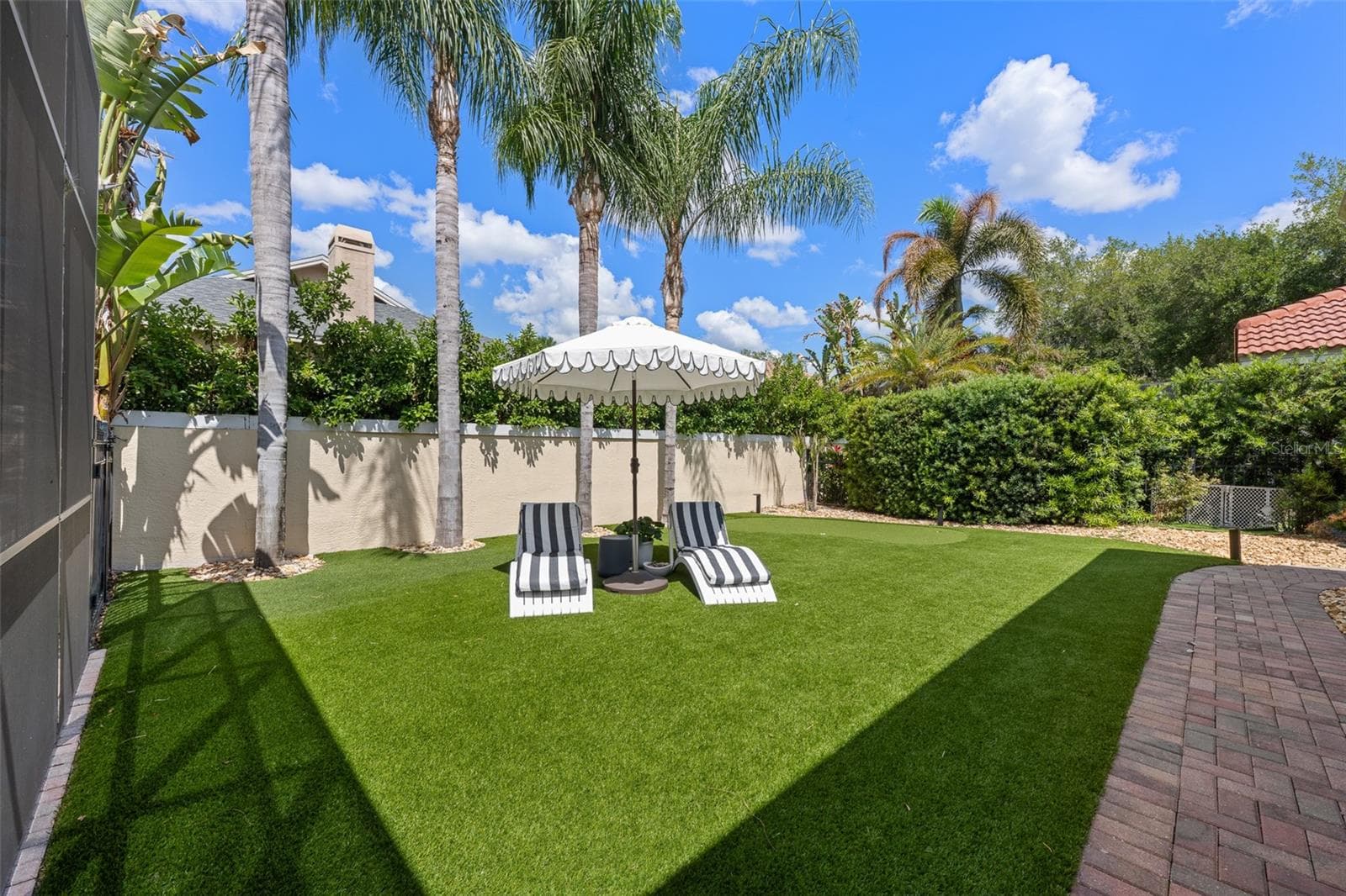 Backyard — Fenced yard with artificial turf, palms, and umbrella lounge seating. - 1921 FLORESTA VIEW DR, TAMPA