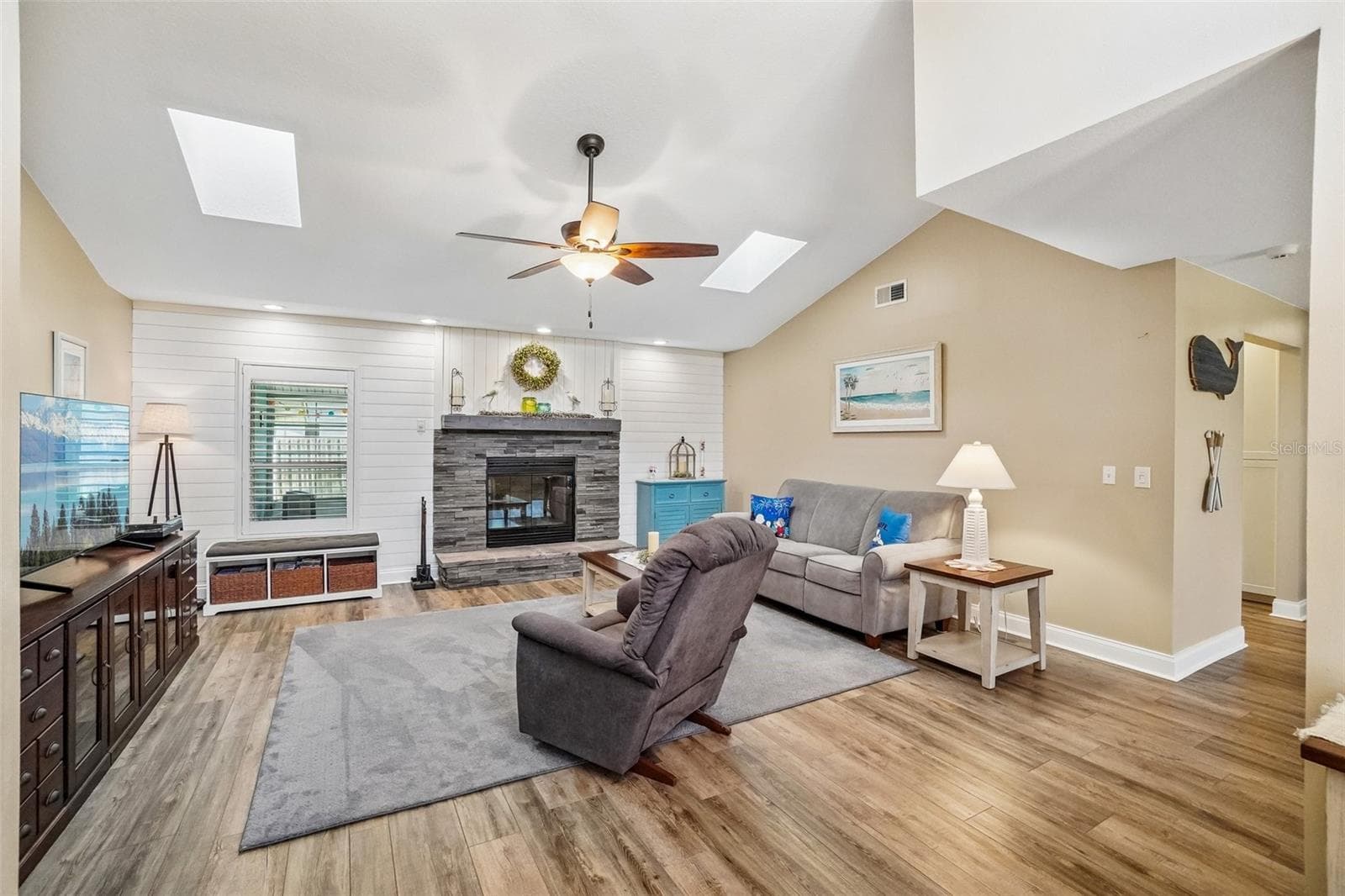 Living Room – The spacious living room features a vaulted ceiling with skylights, wood-look flooring, and a striking stacked-stone fireplace set against a white shiplap accent wall. - 971 CORTLAND WAY, PALM HARBOR
