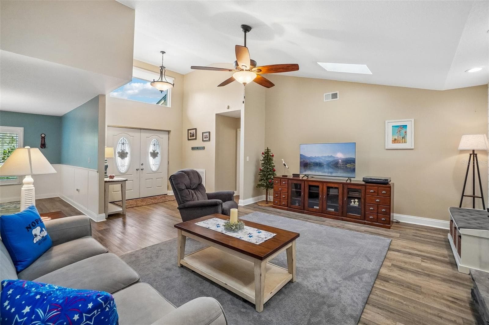 Living Room – This inviting living area offers vaulted ceilings, a skylight, ceiling fan, and generous wall space, with an open connection to the entry and adjacent living areas. - 971 CORTLAND WAY, PALM HARBOR