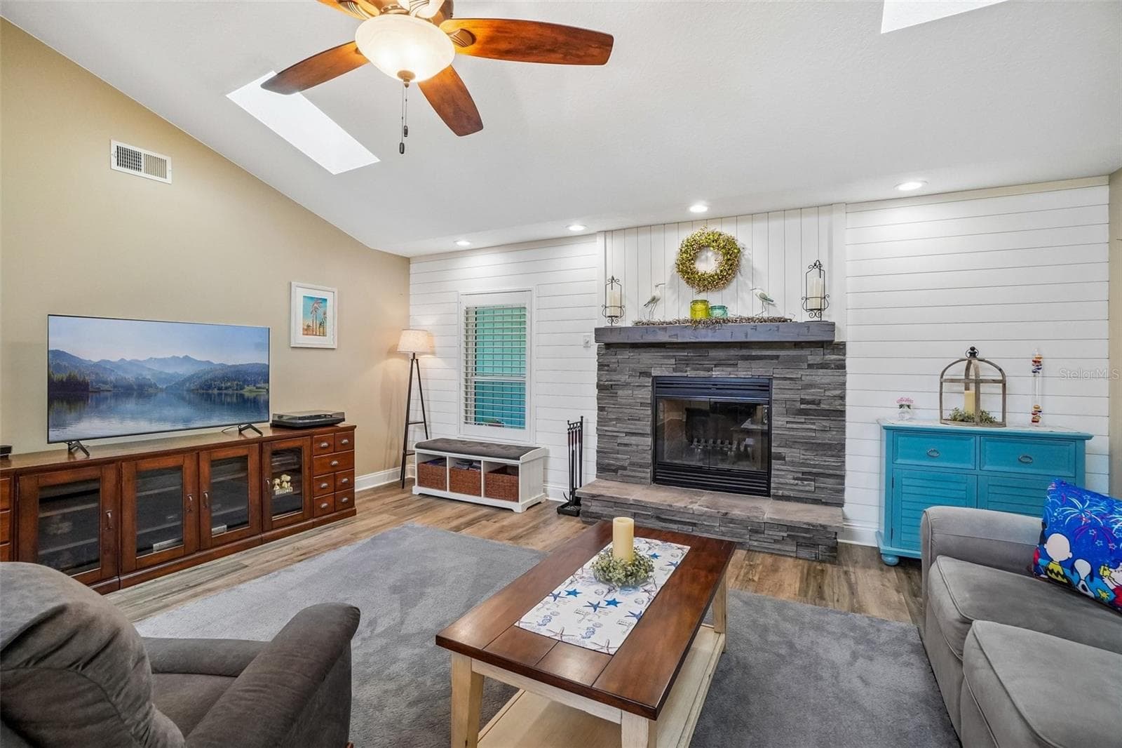 Living Room – A closer view showcases the stacked-stone fireplace and white shiplap accent wall, complemented by wood-look flooring, recessed lighting, and a skylight overhead. - 971 CORTLAND WAY, PALM HARBOR