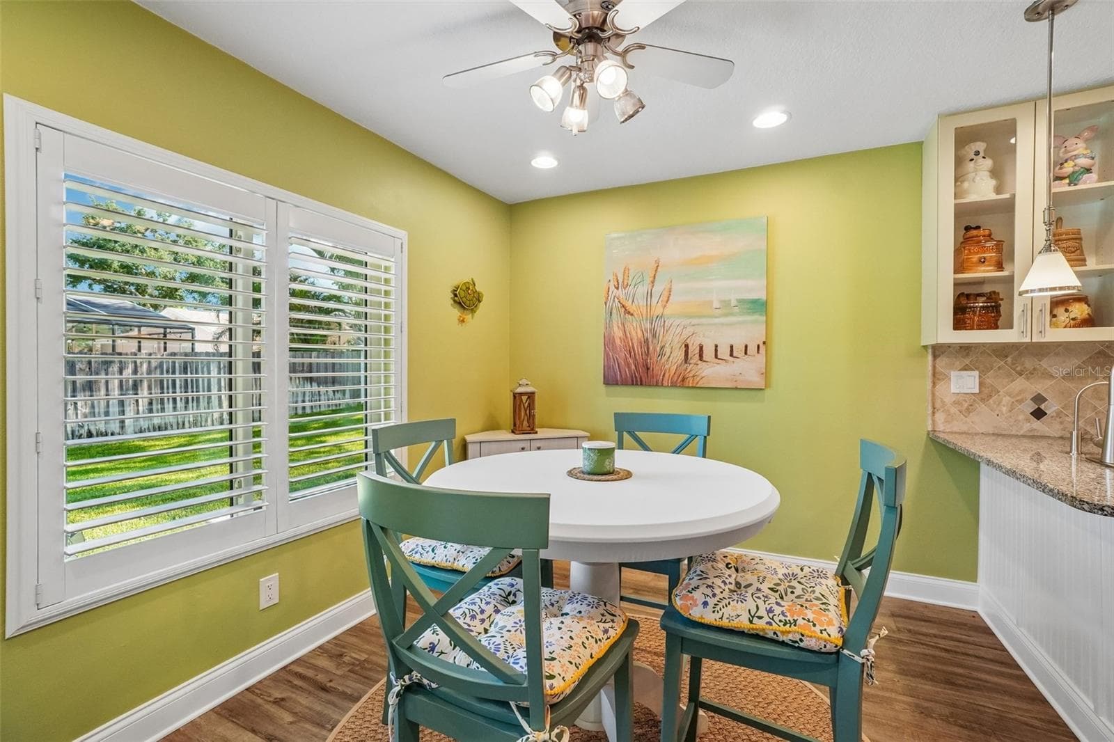 Breakfast Nook – The bright breakfast nook features a large shuttered window overlooking the yard, wood-look flooring, and a ceiling fan, with convenient access to the adjoining kitchen. - 971 CORTLAND WAY, PALM HARBOR