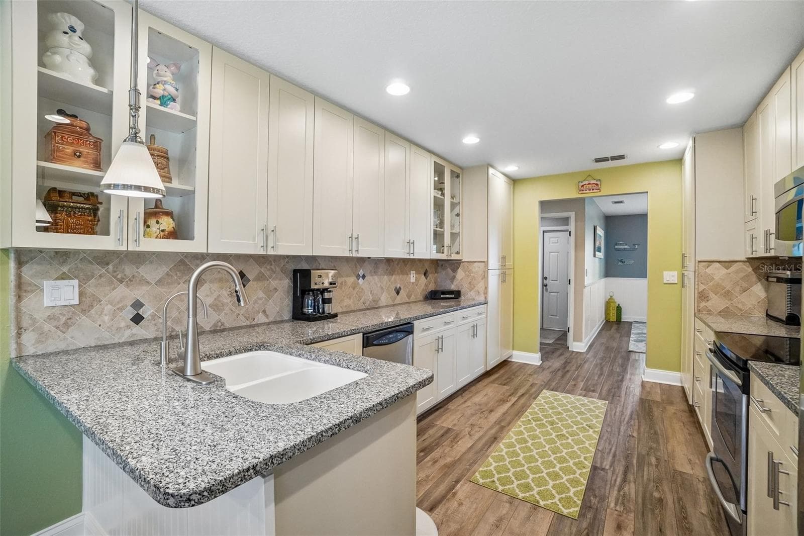 Kitchen – A peninsula with an undermount sink provides additional prep space, while stone countertops, soft cream cabinetry, glass-front display cabinets, a tiled backsplash, and recessed lighting complete the bright kitchen. - 971 CORTLAND WAY, PALM HARBOR