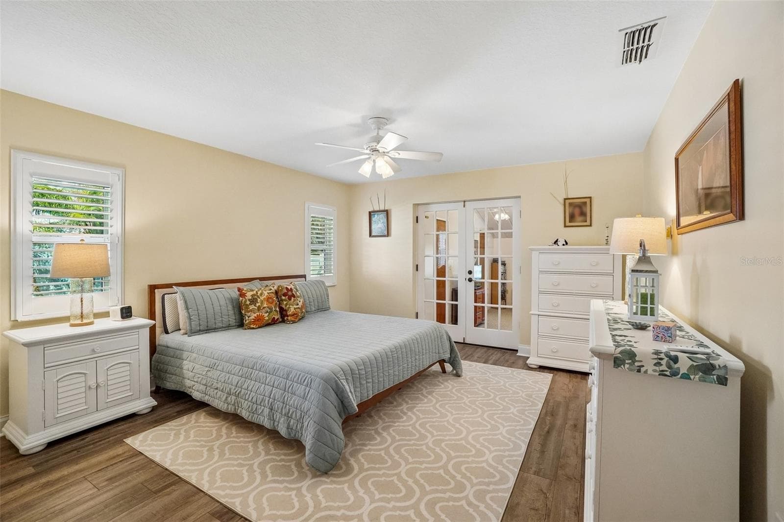 Primary Bedroom – The spacious primary bedroom features wood-look flooring, plantation shutters, a ceiling fan, and French doors that add character while connecting to the adjoining space. - 971 CORTLAND WAY, PALM HARBOR