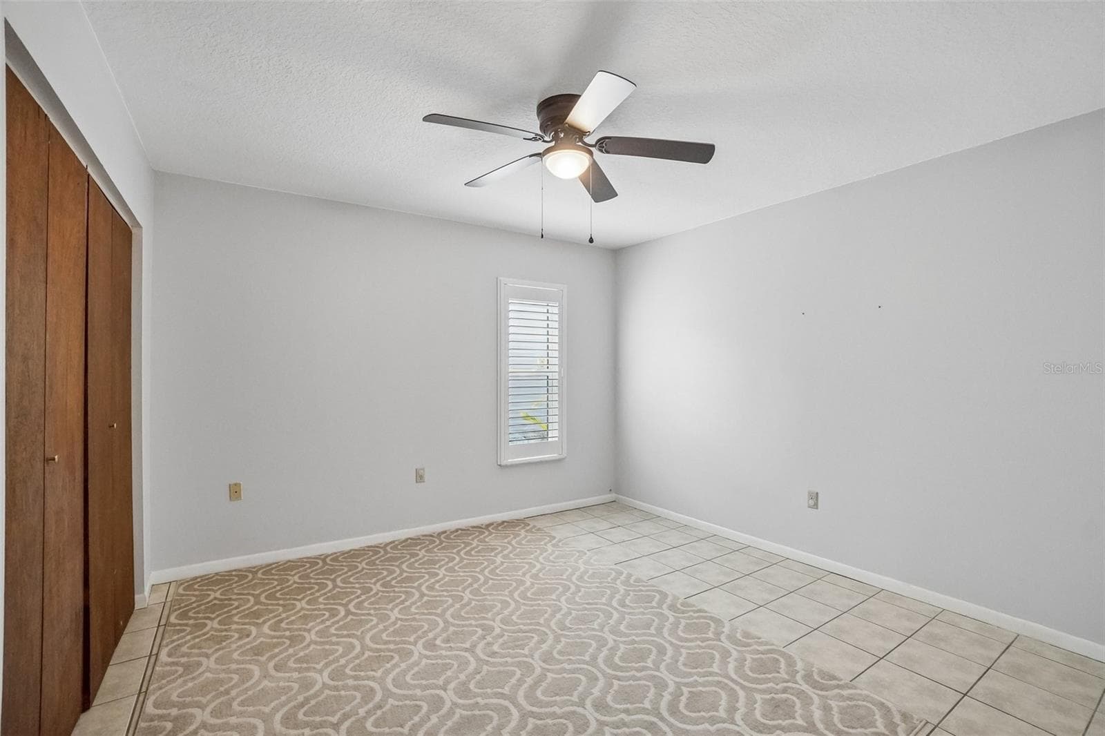 Third Bedroom – The third bedroom offers neutral finishes, tile flooring, a ceiling fan, a plantation-shuttered window, and a wide sliding-door closet for generous storage. - 971 CORTLAND WAY, PALM HARBOR