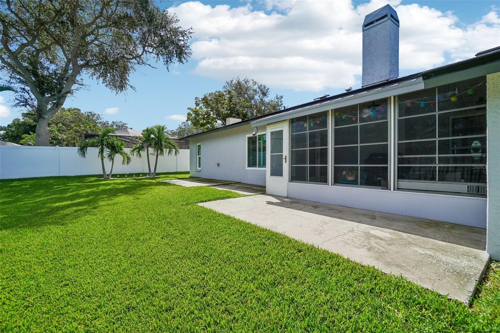 Rear Patio & Backyard – Showcasing the enclosed patio and adjoining concrete patio area, with the manicured lawn and privacy fencing extending beyond. - 971 CORTLAND WAY, PALM HARBOR