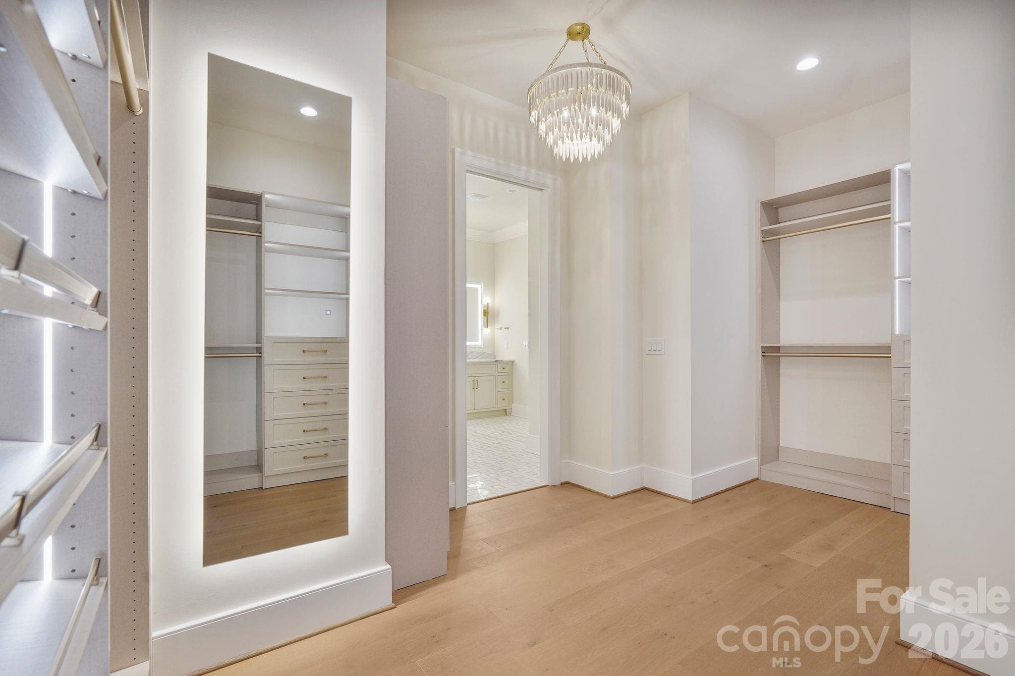 Boutique-inspired primary closet featuring oversized LED mirrors, custom built-ins, and a statement light fixture, creating an elevated space designed for getting ready in style. - 21216 Rio Oro Drive, Cornelius