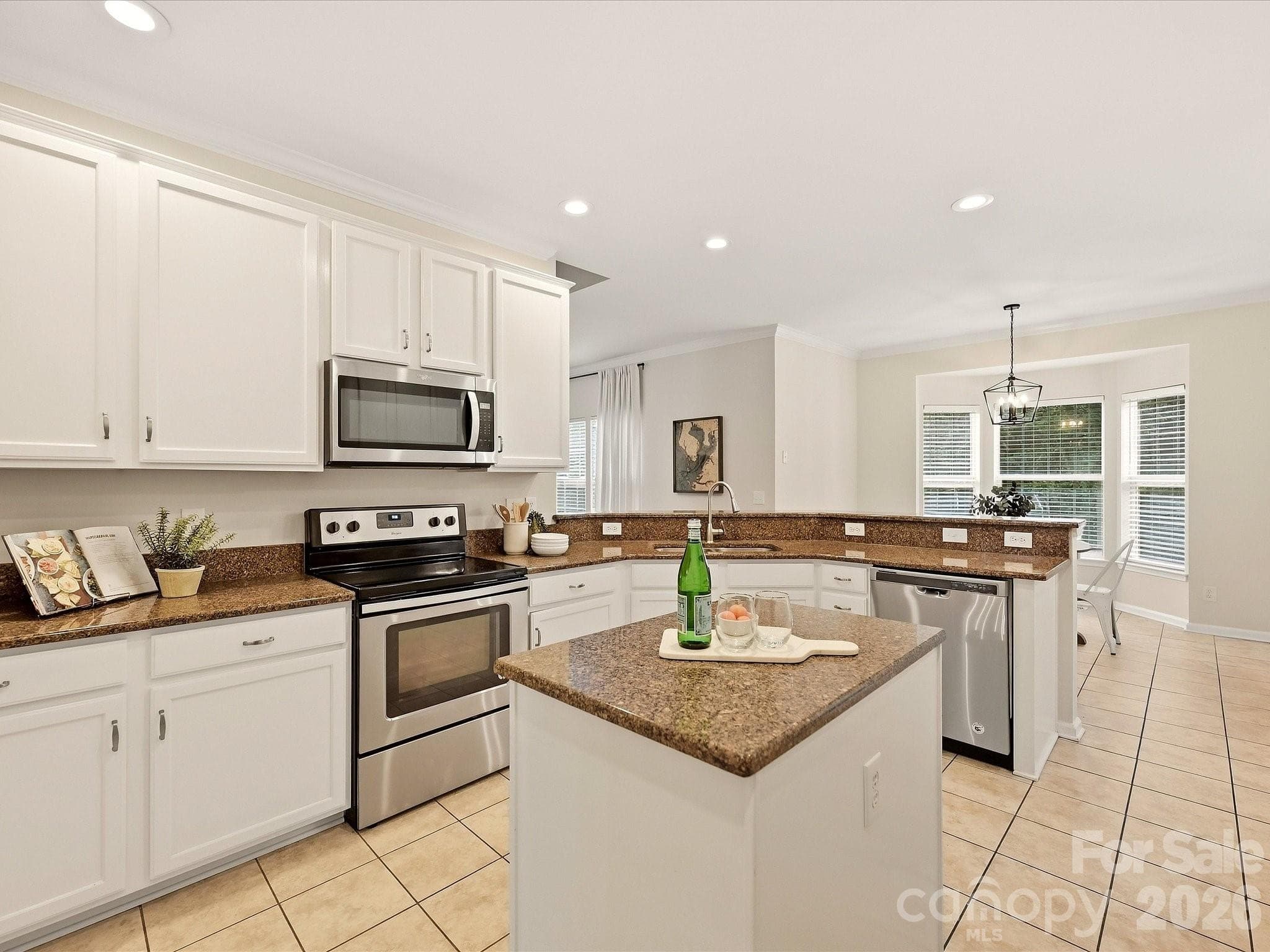 The bright kitchen features crisp white cabinetry, granite countertops, stainless steel appliances, a center island, and an open layout that connects easily to the surrounding living spaces. - 16006 Lavenham Road, Huntersville