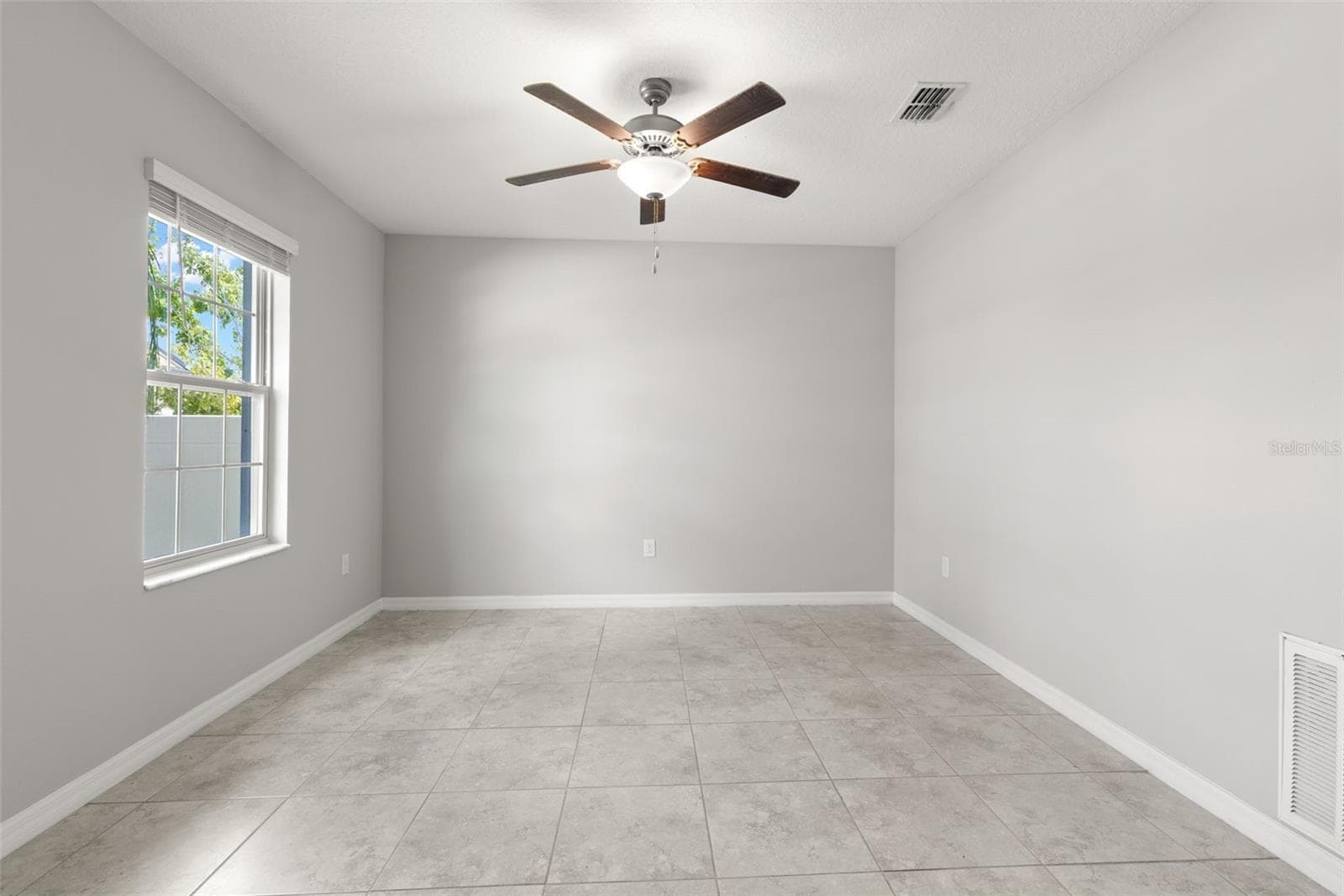The bonus room/office serves as the home’s flexible fifth-bedroom space, with a large window, tile flooring, fresh neutral paint and a ceiling fan; this room does not have a closet. - 5061 WHITE CHICORY DR, APOLLO BEACH