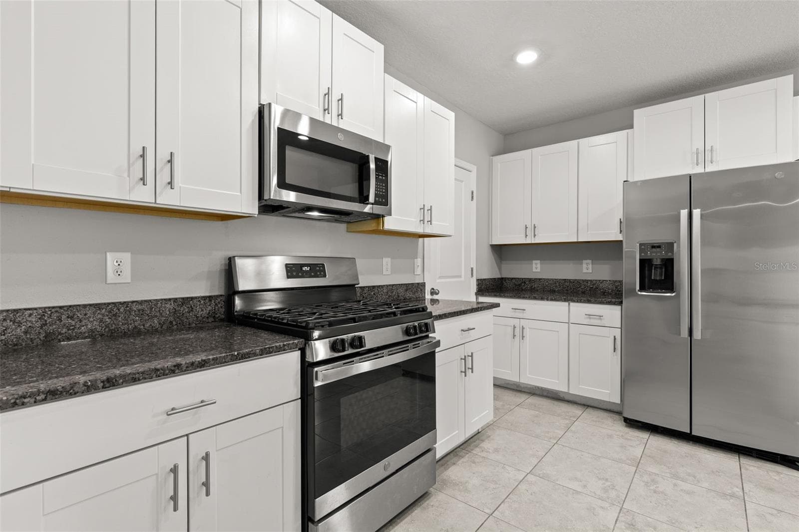 Stainless appliances include a gas range, built-in microwave and French-door refrigerator with ice maker and exterior water dispenser, complemented by white cabinetry and granite countertops. - 5061 WHITE CHICORY DR, APOLLO BEACH