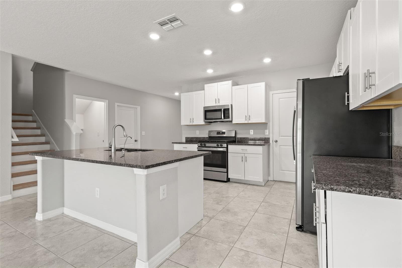 The kitchen combines white shaker-style cabinetry, granite countertops and stainless appliances with a large center island offering generous prep space and room for counter seating. Abundant storage and recessed lighting round out the bright, practical workspace. - 5061 WHITE CHICORY DR, APOLLO BEACH