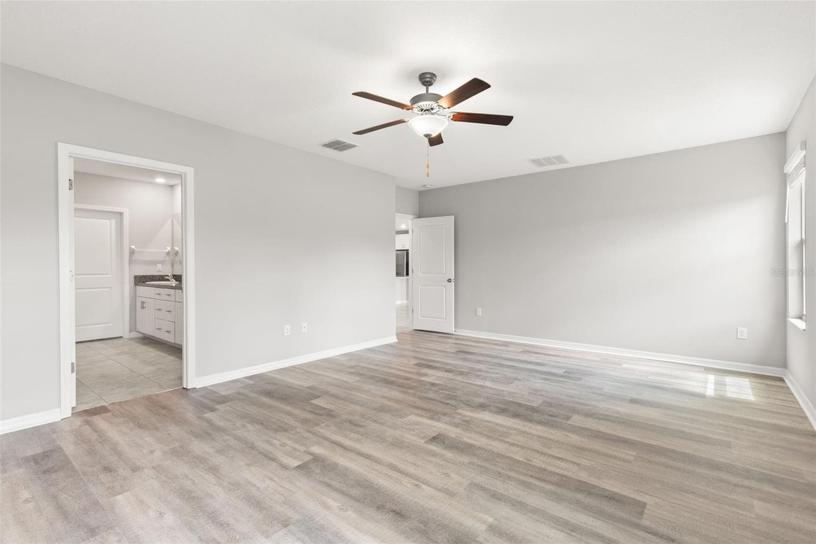 The first-floor primary bedroom connects directly to the ensuite bath, with fresh neutral paint, newly replaced laminate flooring and plenty of space for a full bedroom suite. - 5061 WHITE CHICORY DR, APOLLO BEACH