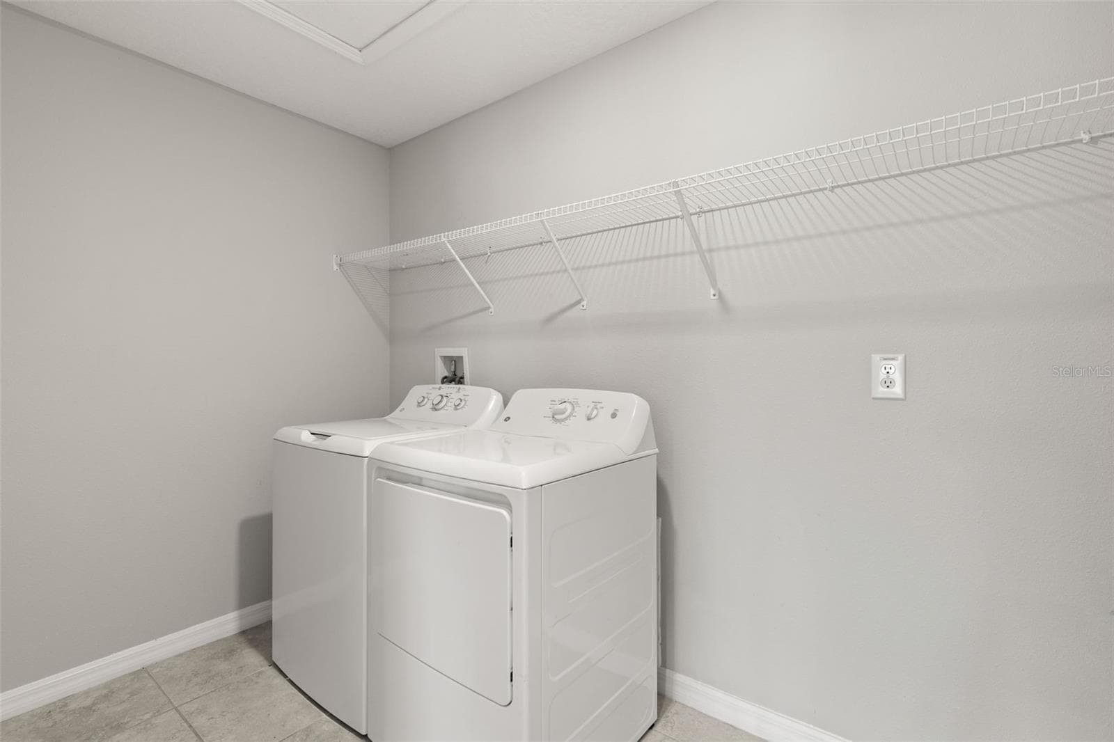 The dedicated laundry room includes a washer and dryer, tile flooring and a long wall-mounted shelf for supplies, linens and extra storage. - 5061 WHITE CHICORY DR, APOLLO BEACH