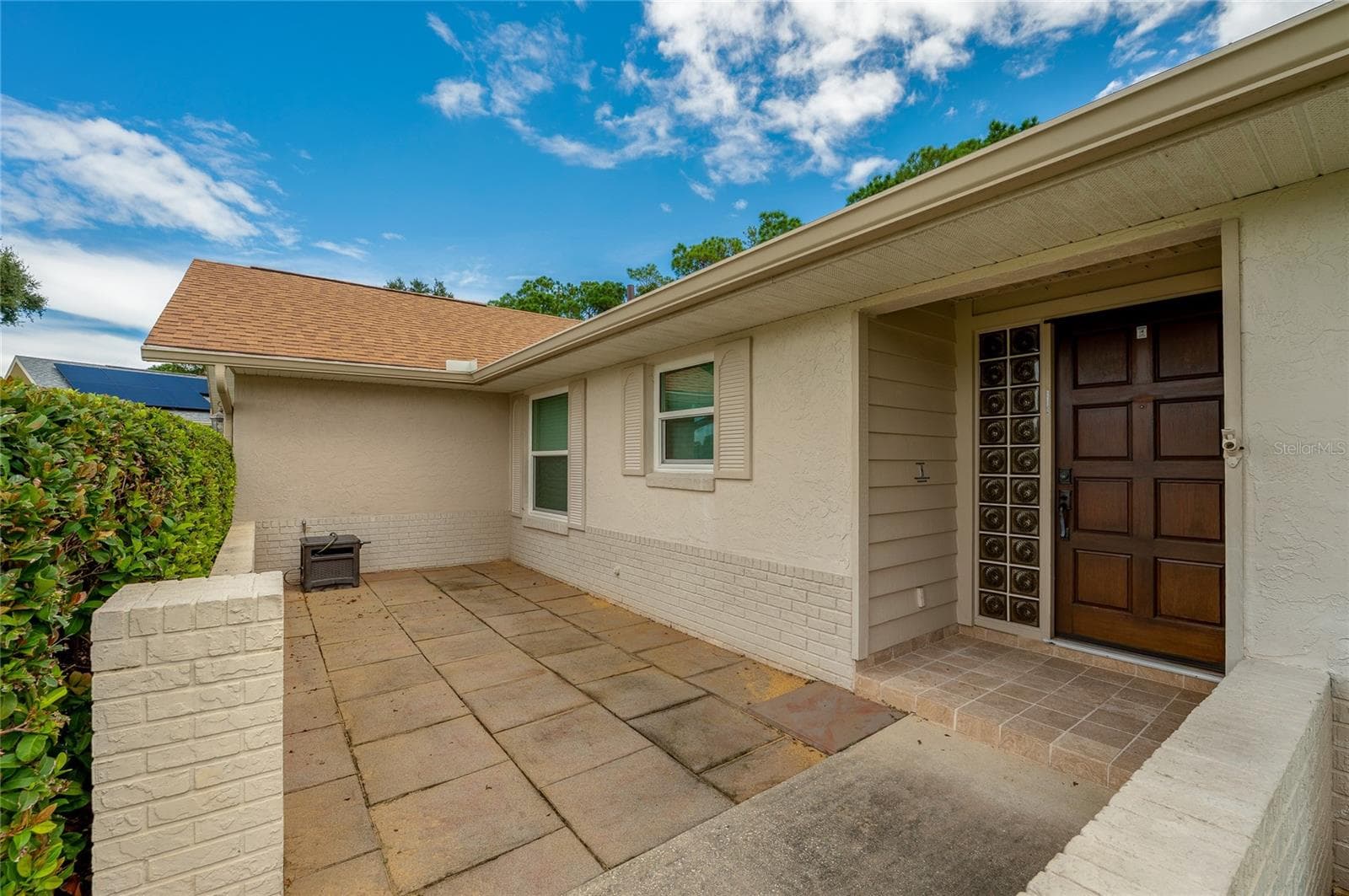 Welcoming front entry patio framed by brick half-walls, tiled walkways, and decorative glass block accents by the door. - 4669 SECRET RIVER TRL, PORT ORANGE