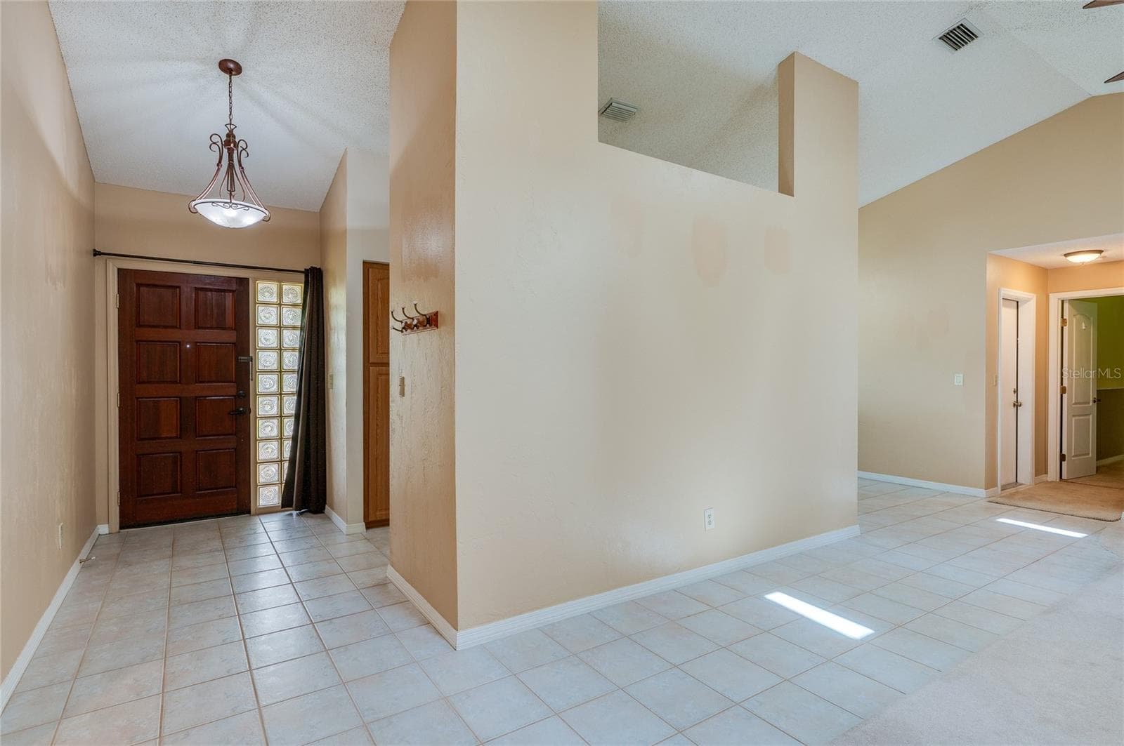 Spacious entry hallway featuring tile flooring, warm neutral walls, and a large decorative wood door with glass block side panels. Vaulted ceilings and open wall cutouts create a light-filled ambiance. - 4669 SECRET RIVER TRL, PORT ORANGE