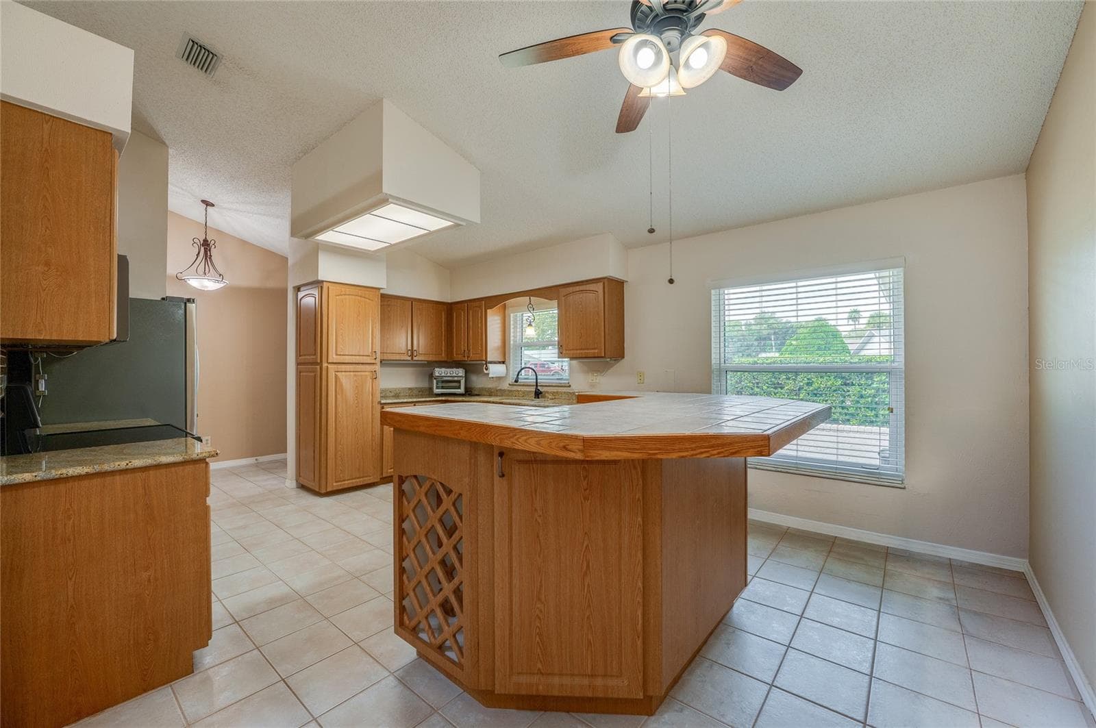 Spacious kitchen displaying warm wooden cabinetry, a tiled center island with built-in wine storage, tile flooring, and a bright window over the sink. - 4669 SECRET RIVER TRL, PORT ORANGE