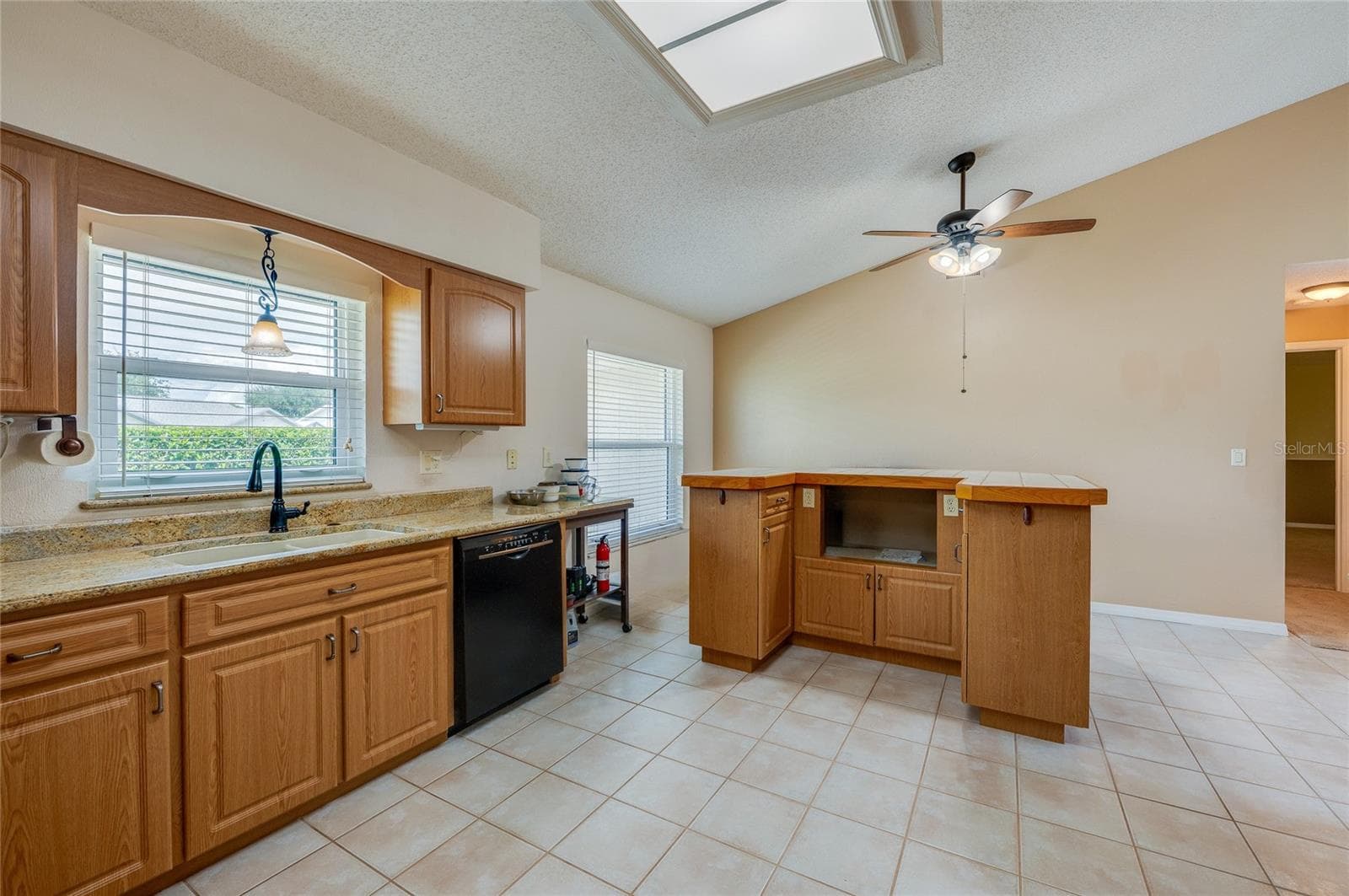 Bright kitchen featuring warm wood cabinetry, neutral countertops, a ceiling fan, and durable tile flooring throughout. - 4669 SECRET RIVER TRL, PORT ORANGE