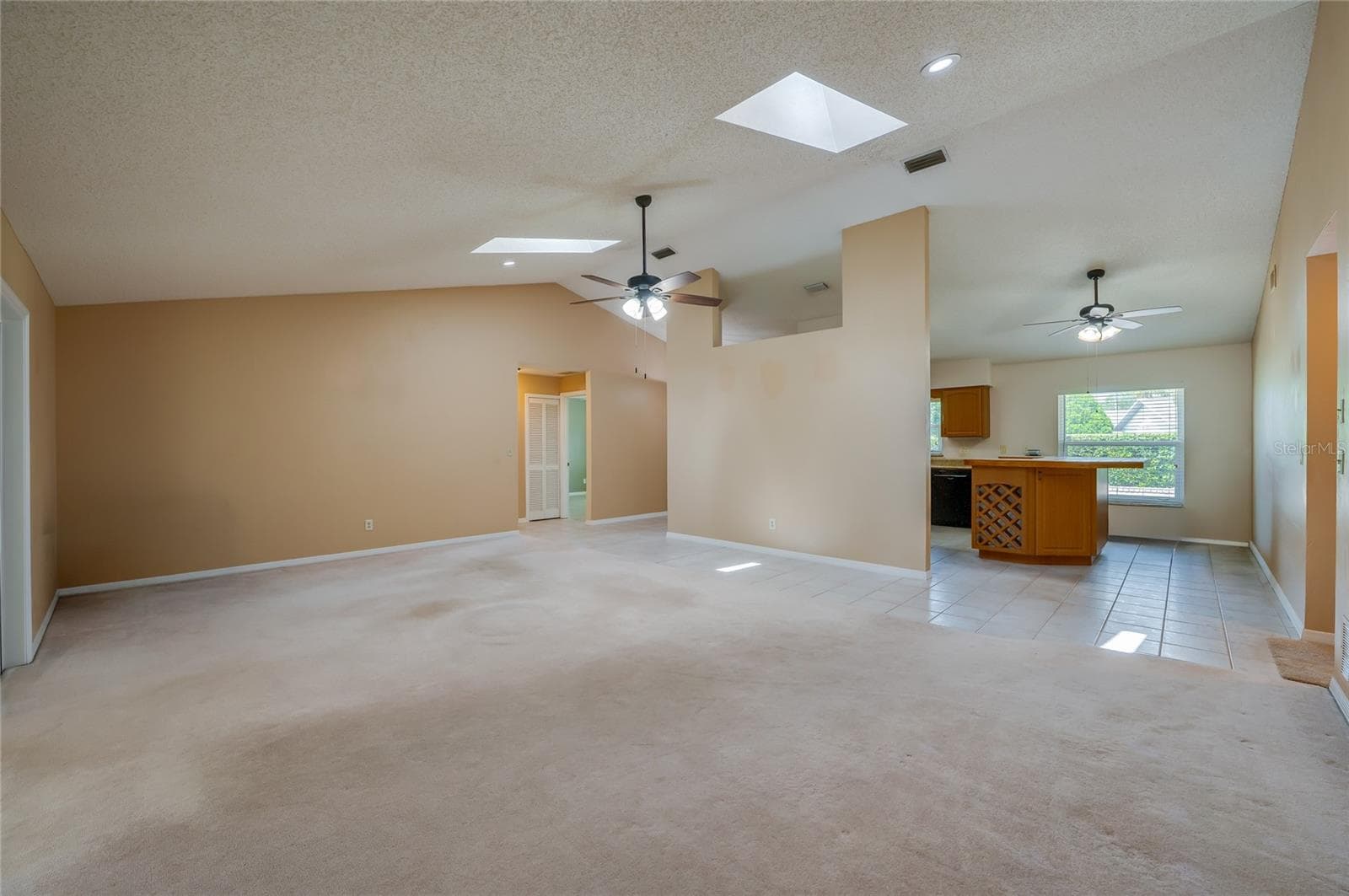 Open-concept living space highlighting high vaulted ceilings, skylights, plush carpeting, and seamless flow into the adjacent tiled kitchen area. - 4669 SECRET RIVER TRL, PORT ORANGE