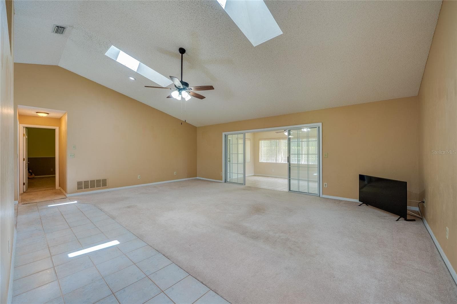 Expansive living room area featuring vaulted ceilings with skylights, carpeted flooring, and sliding glass doors that open to a sun room. - 4669 SECRET RIVER TRL, PORT ORANGE