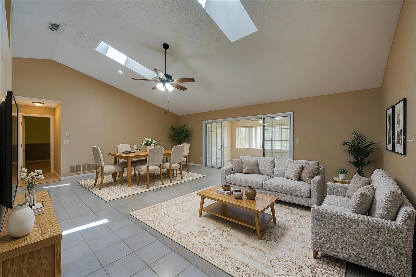 Virtually Staged - Expansive living room area featuring vaulted ceilings with skylights, carpeted flooring, and sliding glass doors that open to a sun room. - 4669 SECRET RIVER TRL, PORT ORANGE