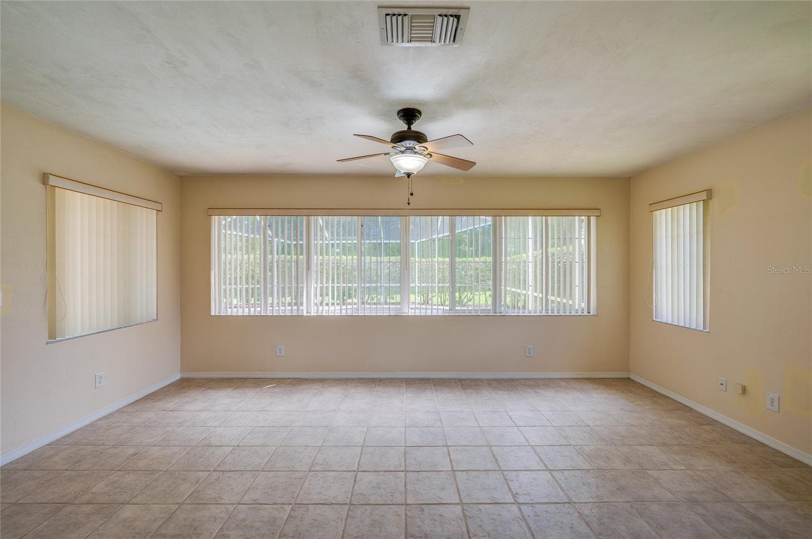 Bright enclosed sunroom equipped with light beige tile flooring, a ceiling fan, and wide windows fitted with vertical blinds for controlled light. - 4669 SECRET RIVER TRL, PORT ORANGE