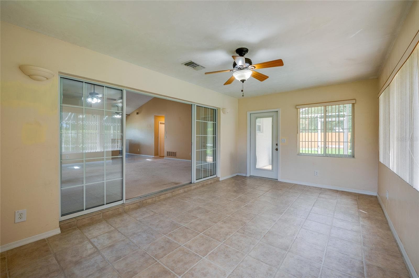 Versatile sunroom space featuring sliding glass entry doors, tile flooring, a ceiling fan fixture, and a exterior door providing outdoor access. - 4669 SECRET RIVER TRL, PORT ORANGE
