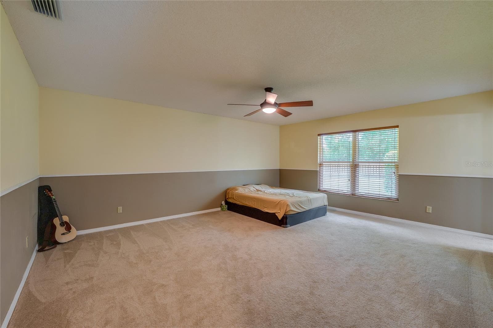 Spacious primary bedroom featuring soft carpeting, two-tone painted walls, a central ceiling fan, and a large window providing pleasant outdoor views. - 4669 SECRET RIVER TRL, PORT ORANGE