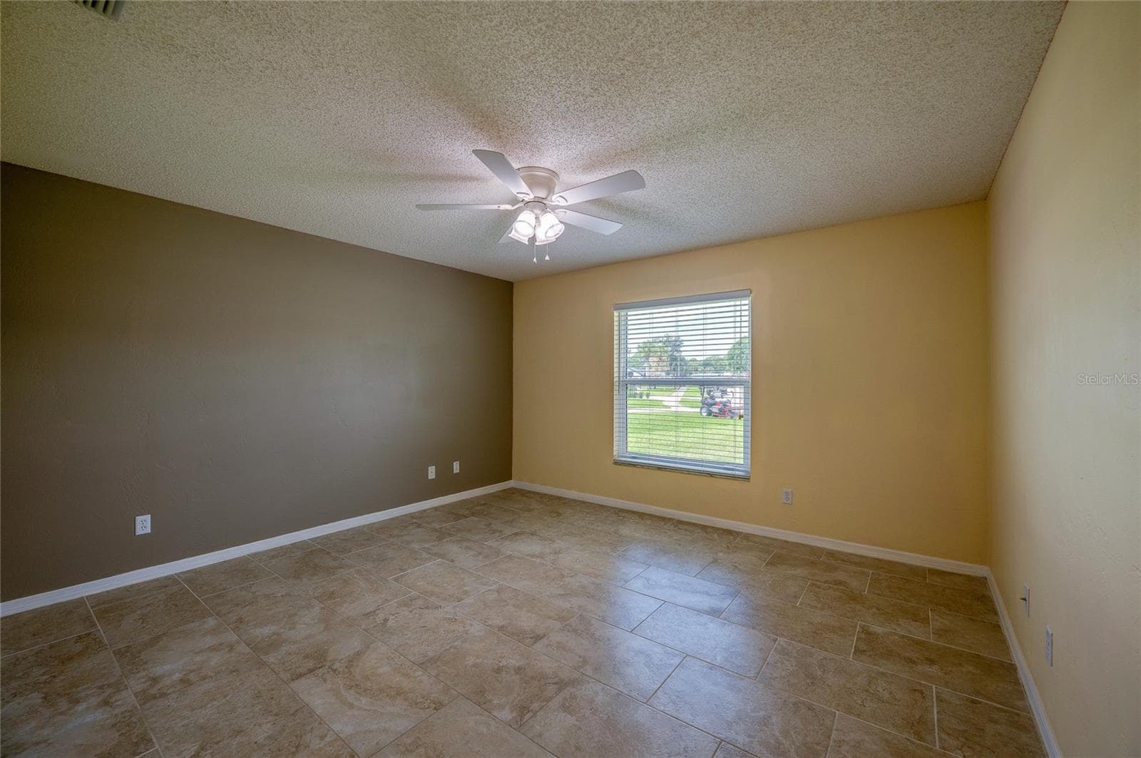 Generous bedroom featuring neutral tiled flooring, dual-tone walls, and a central ceiling fan with integrated lighting. Large window with blinds allows for ample natural light. - 4669 SECRET RIVER TRL, PORT ORANGE