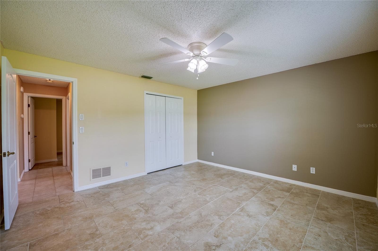 Spacious room showcasing easy-to-clean tile flooring, double closet doors, and an open doorway leading to adjacent hall spaces. - 4669 SECRET RIVER TRL, PORT ORANGE