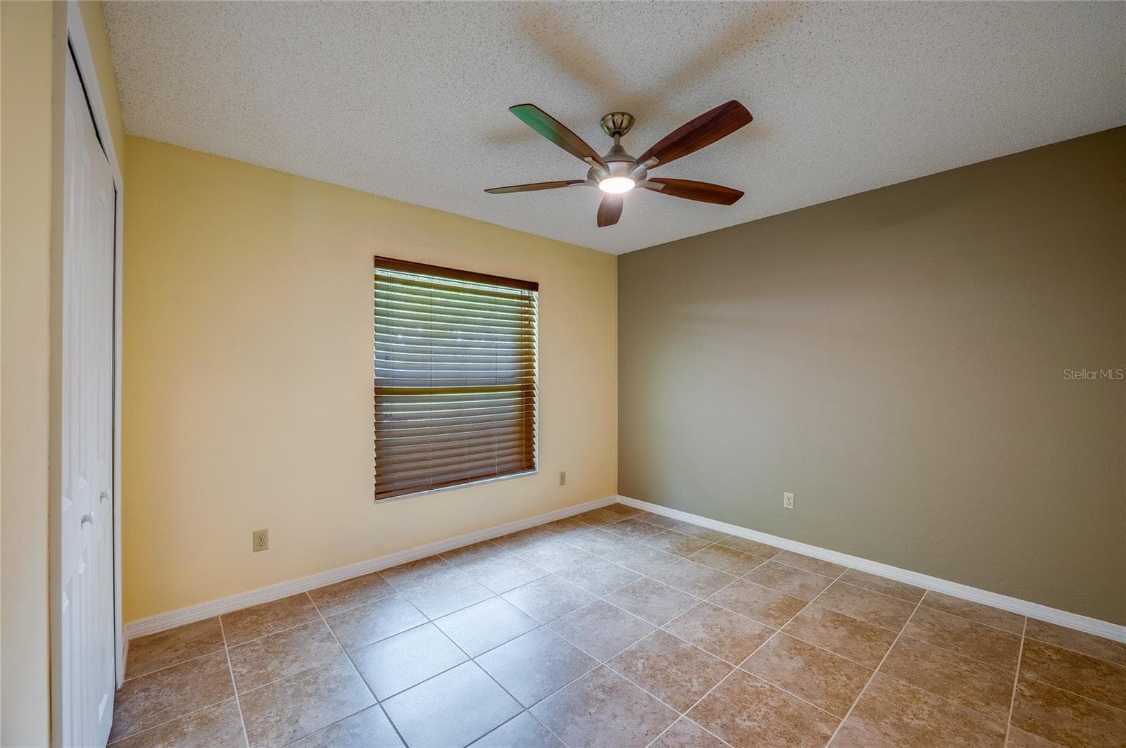 Cozy bedroom offering neutral tile floors, warm wall tones, a modern ceiling fan, and built-in closet space. Window blinds provide light control and privacy. - 4669 SECRET RIVER TRL, PORT ORANGE