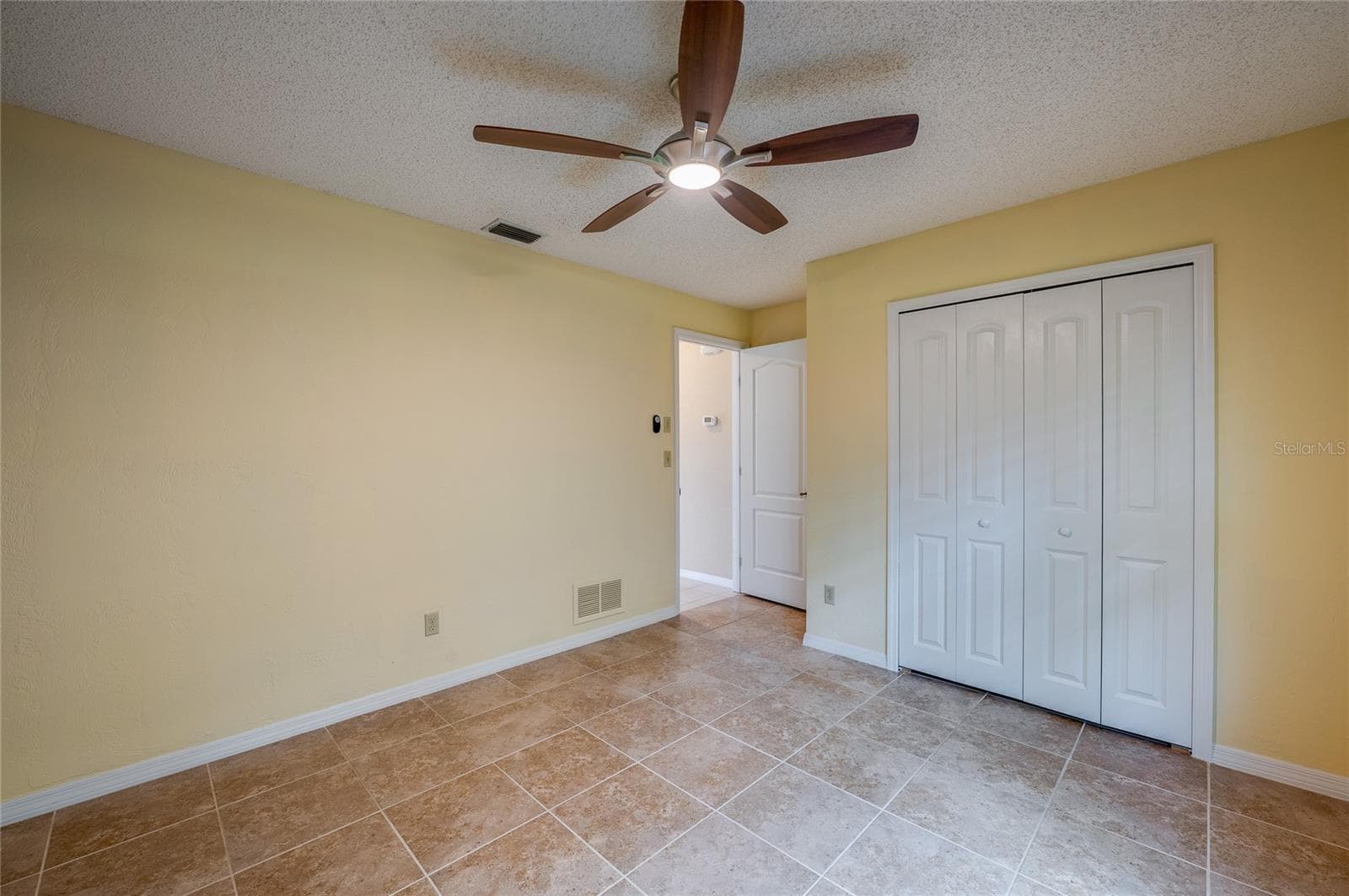 Light-filled bedroom highlighting tiled flooring, smooth neutral walls, and double closet doors for storage. Ceiling fan fixture ensures comfortable airflow. - 4669 SECRET RIVER TRL, PORT ORANGE