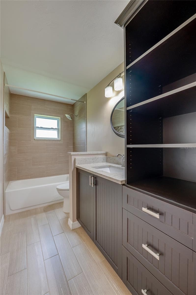 Full bathroom with modern tile flooring, custom dark cabinetry, and open storage. A tiled tub-and-shower combo and elegant wall lighting complete the space. - 4669 SECRET RIVER TRL, PORT ORANGE